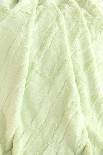 A close-up of a pale mint green Minky Couture Sorbet Lemon Lime faux fur fabric with soft, crinkled vertical folds.