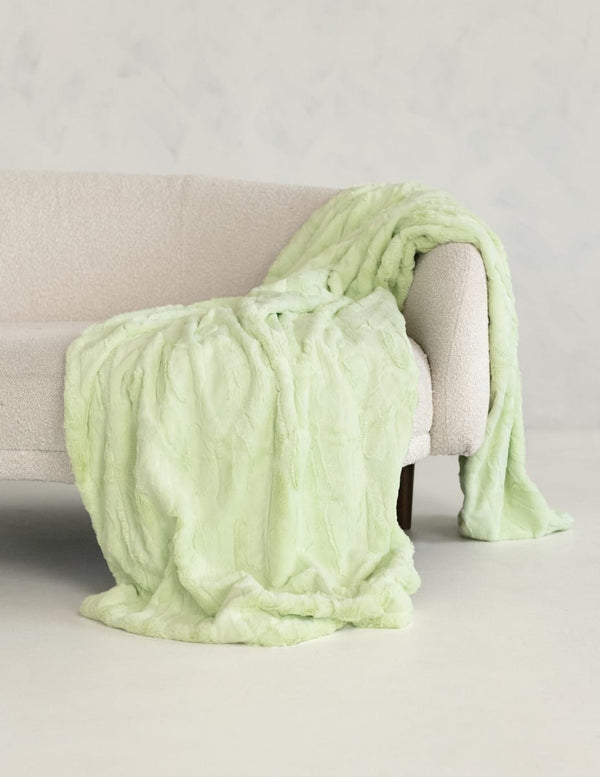 A Minky Couture Sorbet Lemon Lime textured throw blanket draped over a cream-colored armchair in a minimalist room setting.
