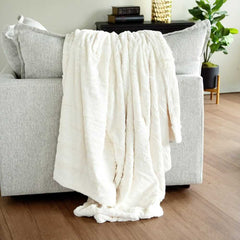 Cream Minky Couture blanket draped over a light gray sofa, showing its soft plush texture.