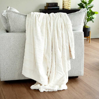 Cream Minky Couture blanket draped over a light gray sofa, showing its soft plush texture.