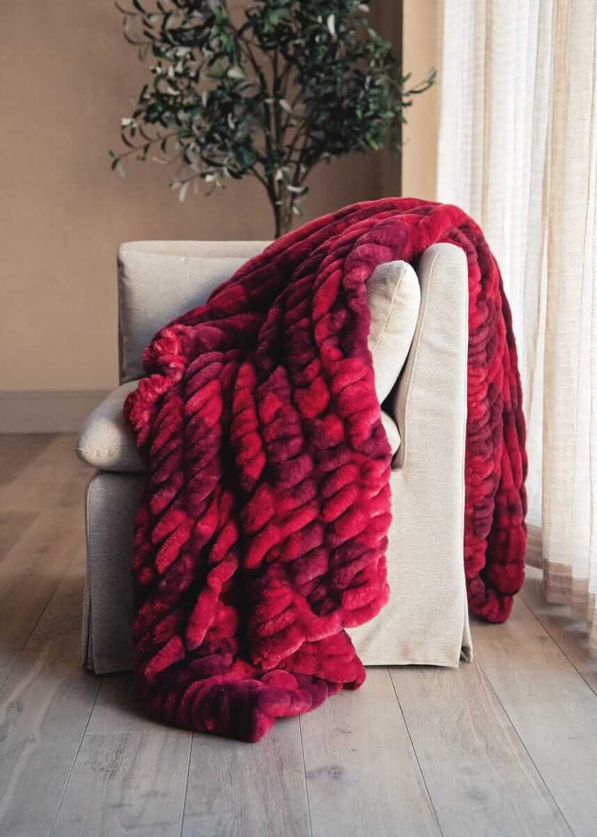 Hugs Diamond Red patterned blanket draped over a beige armchair in a room with a plant and window.