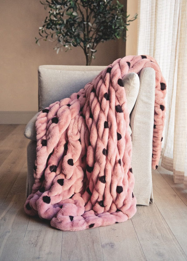 Pink blanket with black dots draped over a chair in a room with a plant and window.