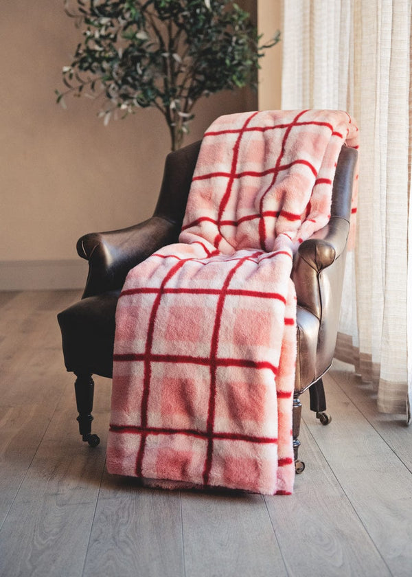Pink and red plaid blanket draped over a brown leather armchair in a room with a plant and curtains.