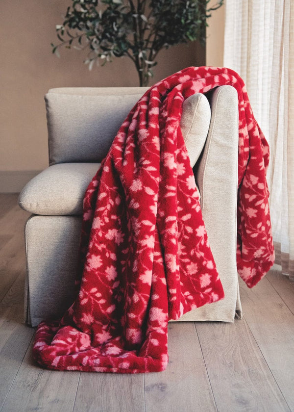 Red floral blanket draped over a beige sofa in a living room setting.