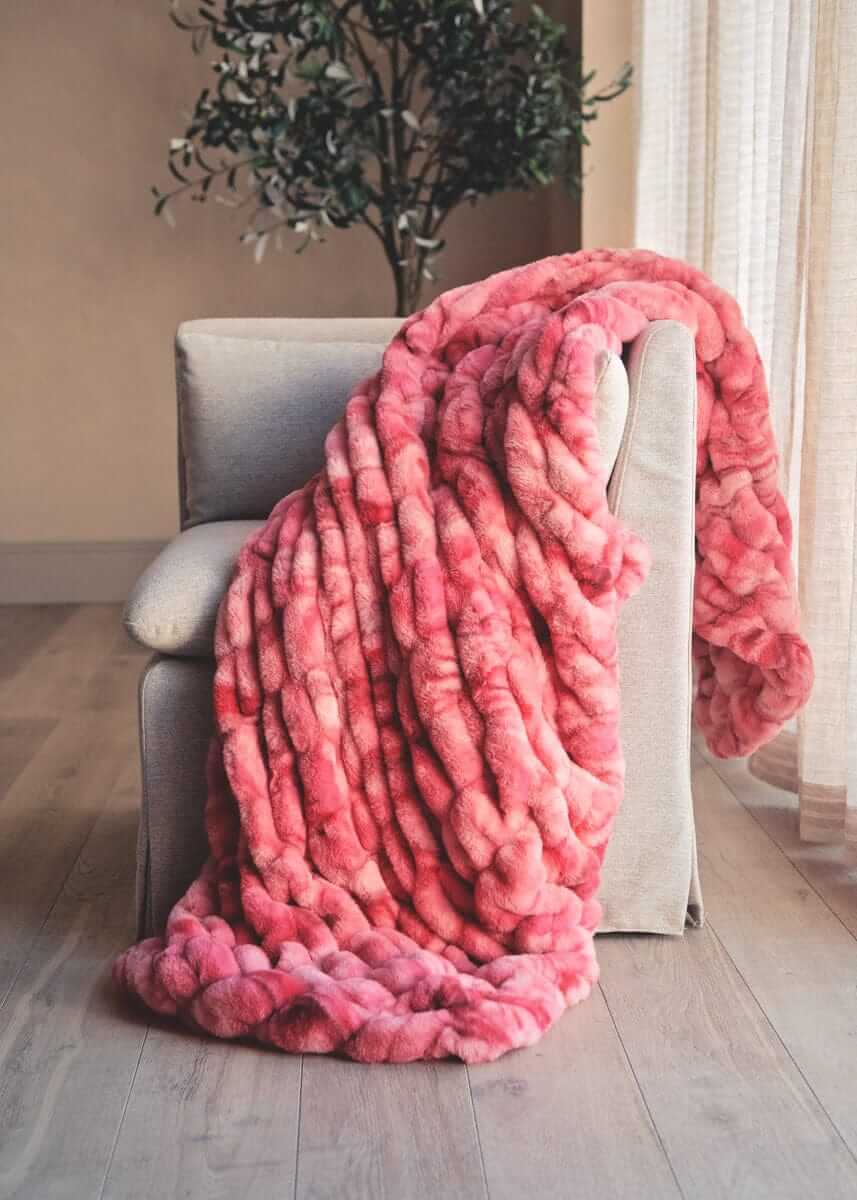 Hugs Raspberry Swirl blanket draped over a chair in a room with a plant and window.
