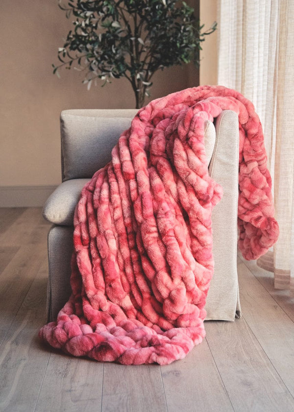 Pink textured blanket draped over a chair in a room with a plant and window.