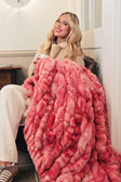 Woman sitting on a couch with a pink Hugs Raspberry Swirl blanket.