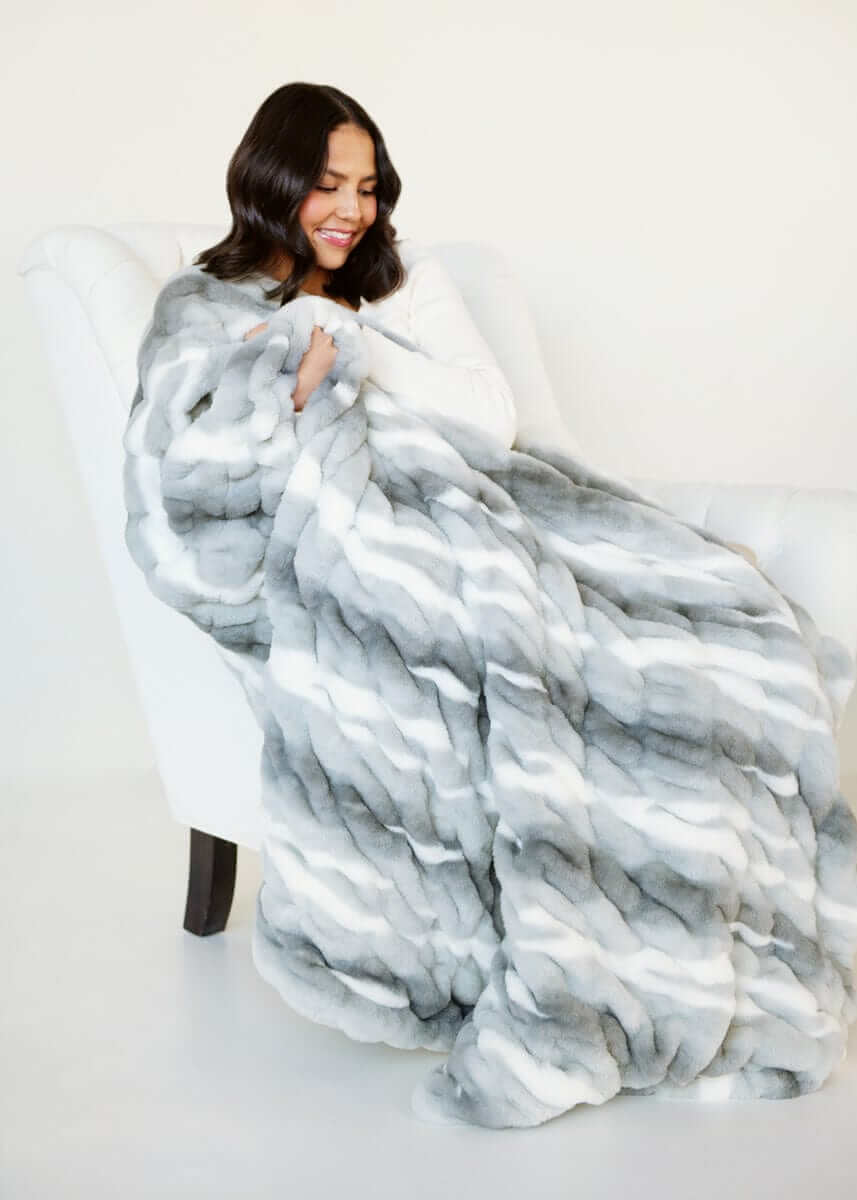 Woman relaxing with White Glove Hugs Swirl Licorice Minky Couture blanket on a white chair.