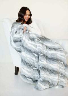 Woman relaxing with White Glove Hugs Swirl Licorice Minky Couture blanket on a white chair.