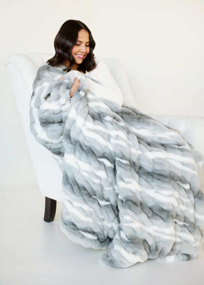 Woman relaxing with White Glove Hugs Swirl Licorice Minky Couture blanket on a white chair.