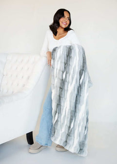 Hugs Swirl Licorice Blanket displayed by a smiling woman, showcasing its plush texture and calming gray stripes.
