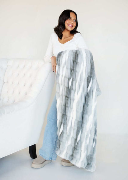 Hugs Swirl Licorice Blanket displayed by a smiling woman, showcasing its plush texture and calming gray stripes.
