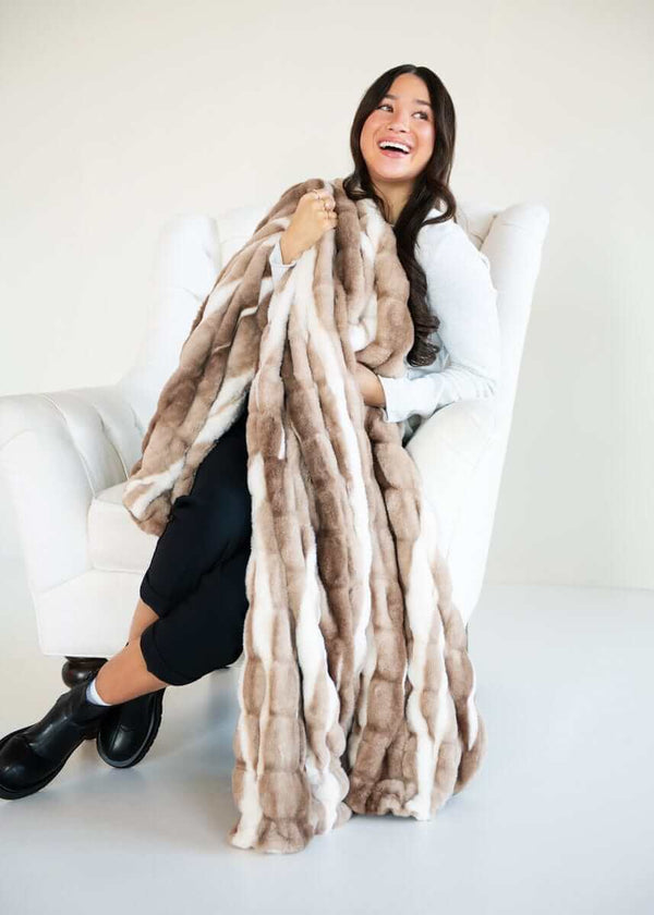 A happy woman wrapped in a White Glove Hugs Swirl Hot Chocolate blanket, showcasing its luxurious design.