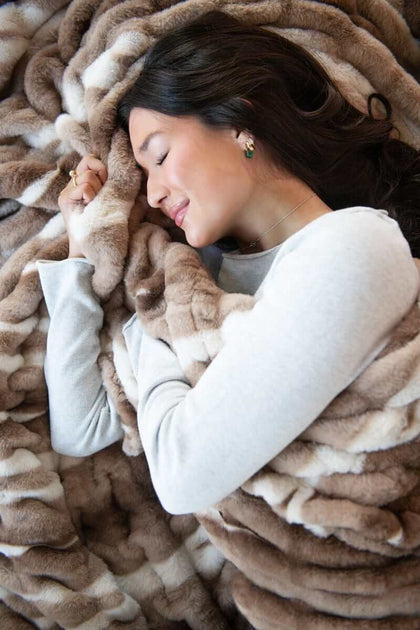 A woman enjoys comfort and warmth wrapped in the Hugs Swirl Hot Chocolate Blanket with brown stripes.