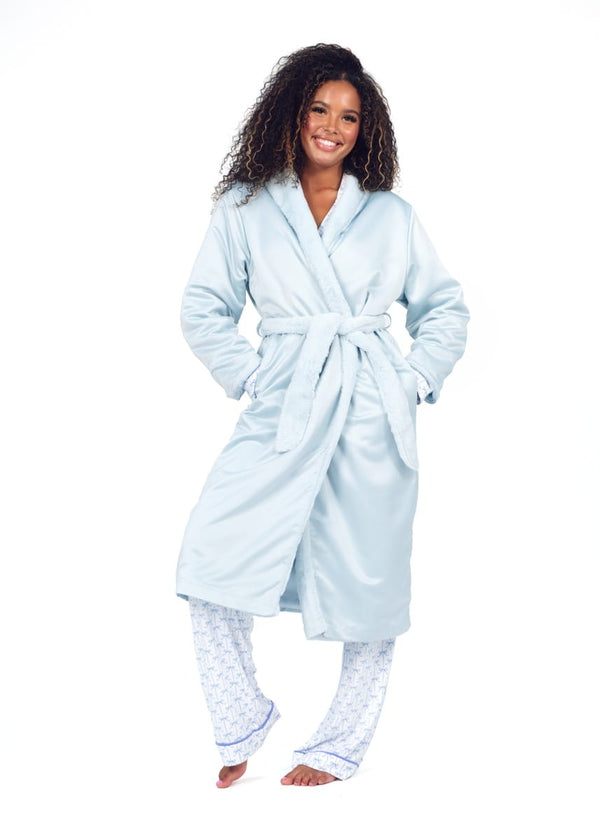 A woman modeling a light blue bathrobe with a matching tie belt, paired with white patterned pajama pants, against a solid white background.
