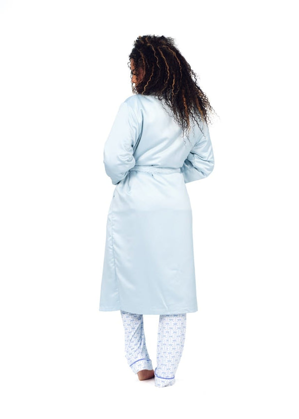 A woman shown from the back wearing a light blue satin-like robe over patterned pajama pants, isolated on a white background.