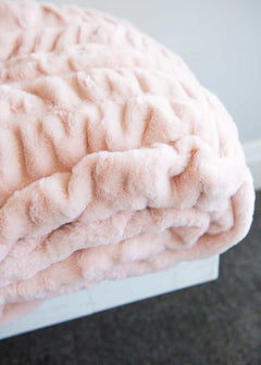 Minky Hugs Peach Whip Blanket on a bed, showcasing its soft texture and light peach color for cozy relaxation.