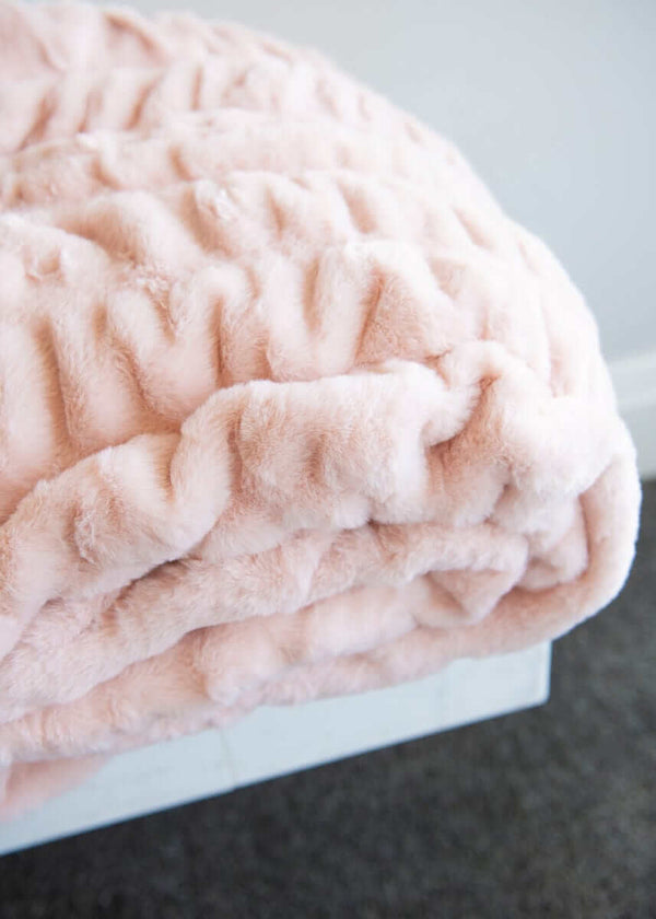 Minky Hugs Peach Whip Blanket on a bed, showcasing its soft texture and light peach color for cozy relaxation.