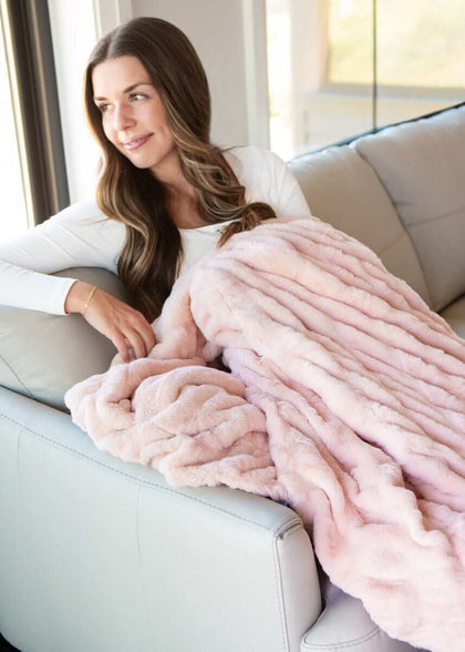 Woman wrapped in Hugs Peach Whip Blanket, enjoying comfort on a couch with soft light peach fabric.