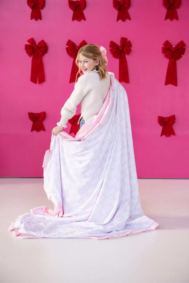Girl in a cozy blanket with Pink Ribbon Bows design against a pink backdrop with bows.