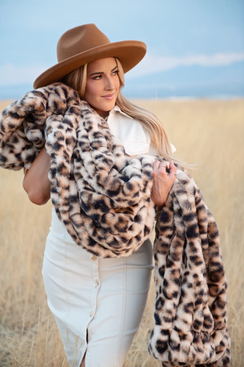Woman in a hat holding a Hugs Golden Leopard Blanket, showcasing its faux fur design in a field.
