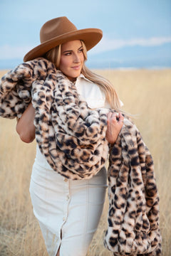 Woman in a hat holding a Hugs Golden Leopard Blanket, showcasing its faux fur design in a field.
