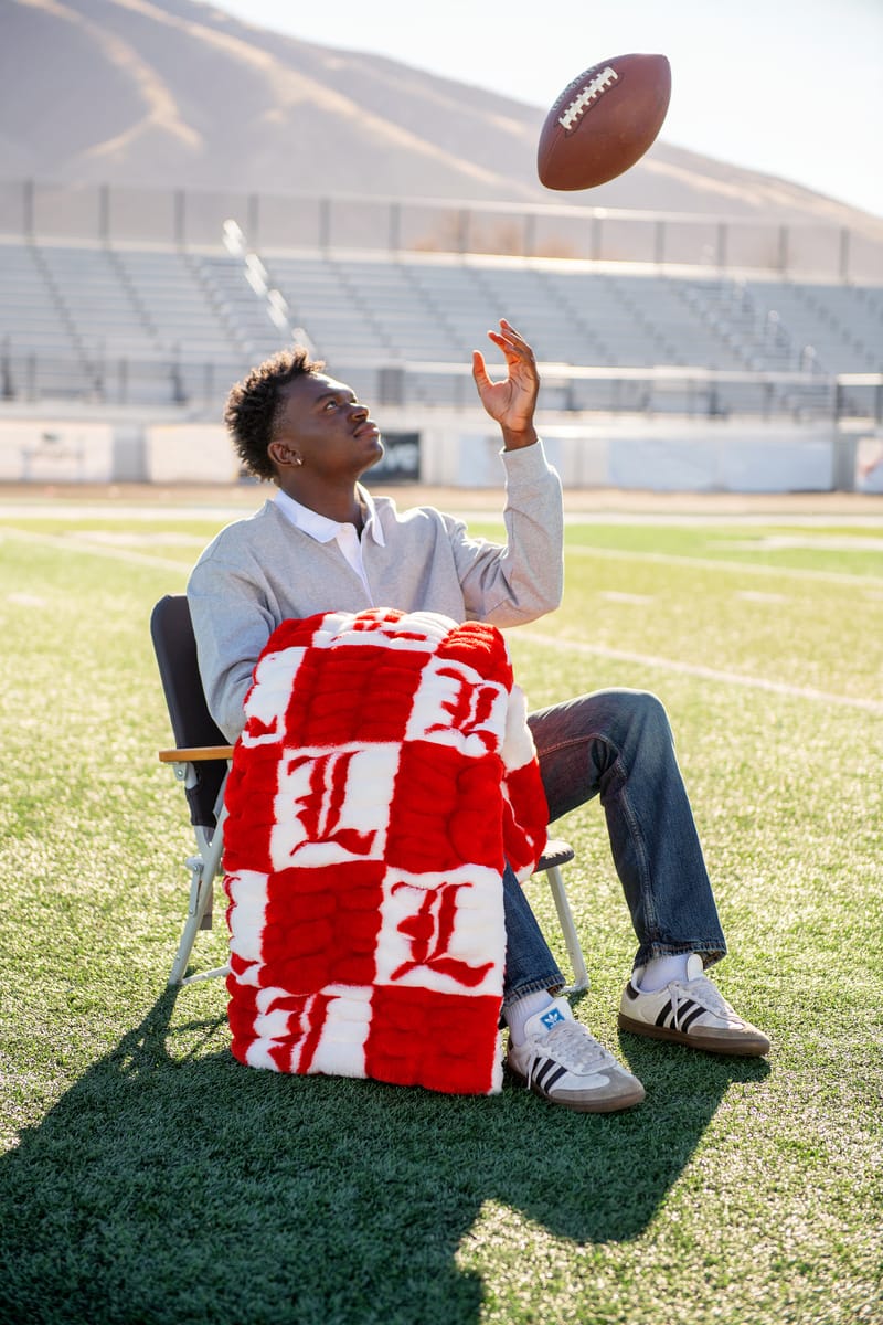 Hugs University of Louisville Blanket displayed on a chair with a football being tossed on the field.