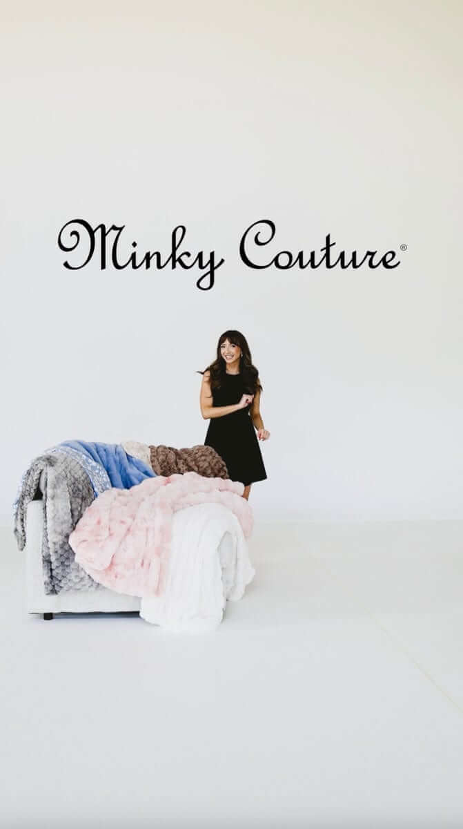 A woman smiling beside a luxurious display of Minky Couture blankets in various colors against a bright background.