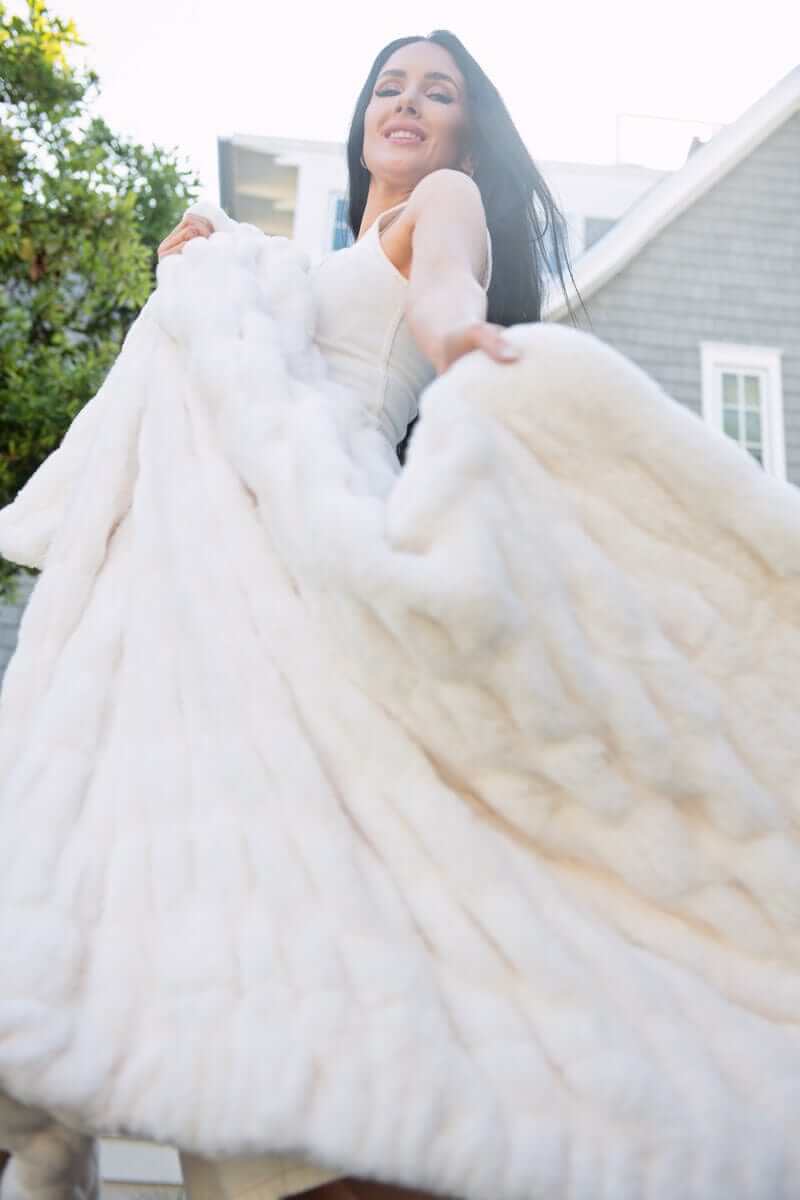 Woman holding a cream Minky Couture weighted blanket outdoors, oversized drape and ultra-soft texture.