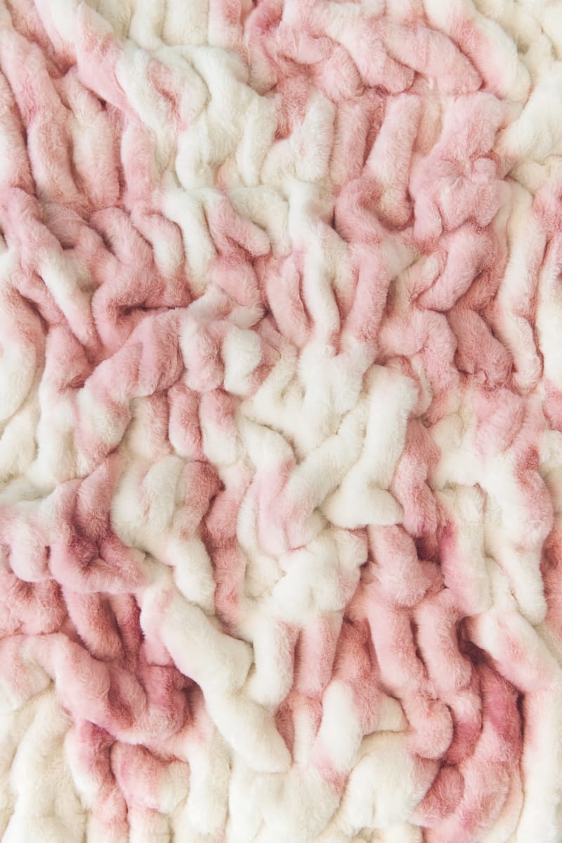A close-up of a Minky Couture textured plush blanket or throw in a soft pink and off-white colorway.