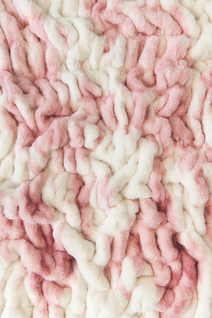 A close-up of a Minky Couture textured plush blanket or throw in a soft pink and off-white colorway.