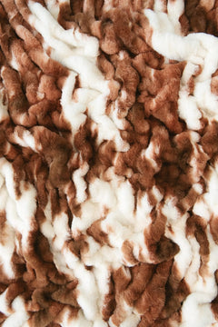 A close-up of a plush minky fabric with a brown and white cow hide pattern.