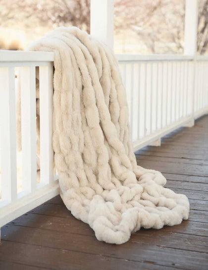Hugs Sugar Cookie Blanket draped over a railing, showcasing its plush, cozy texture and soft neutral tones.