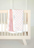 Pink and white Checkered Blush Minky Couture baby blanket draped over a light wood crib railing.