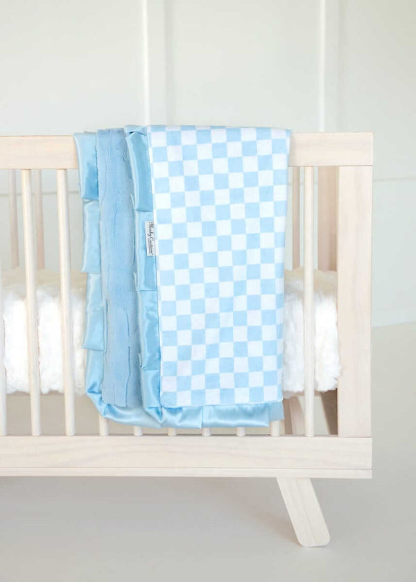 Minky Couture blue and white checkered baby blanket draped over a light wood crib.