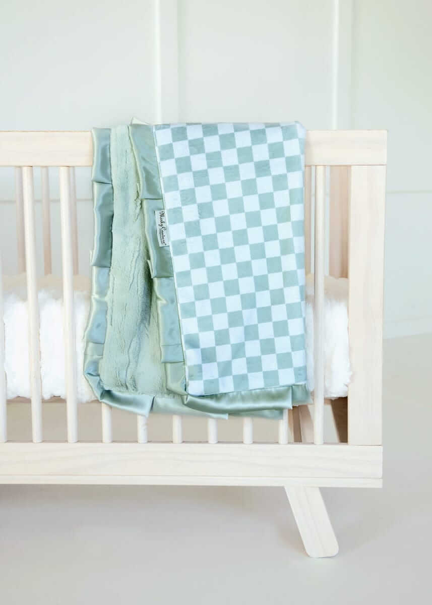 Minky Couture blue and white Checkered Cactus baby blanket draped over a light wood crib.
