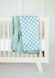 Minky Couture blue and white Checkered Cactus baby blanket draped over a light wood crib.