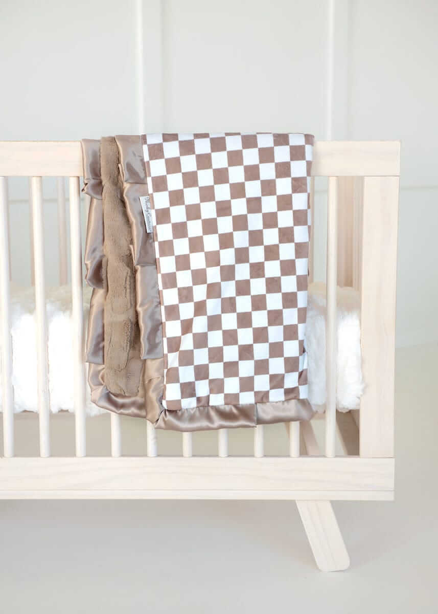 Minky Couture brown and white Checkered Milk Chocolate baby blanket draped over a light wood crib.
