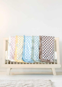 Minky Couture checkered baby blankets in soft pastel colors draped across a light wood crib.