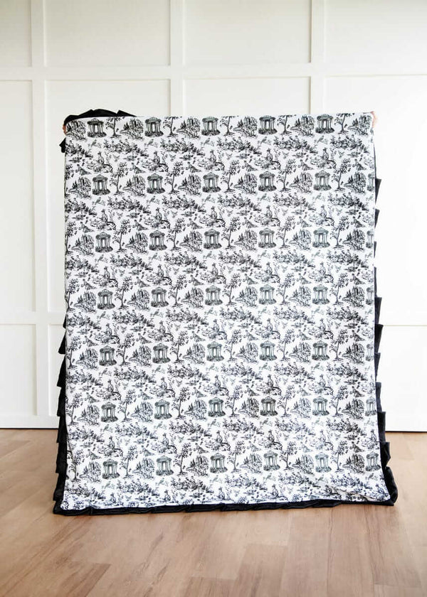 Toile black and white patterned blanket on a wooden floor with a white wall background.