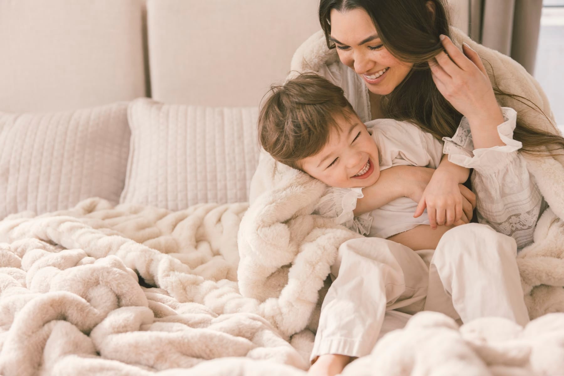 Woman and child snuggling under a blanket on a bed