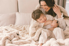 Woman and child snuggling under a blanket on a bed