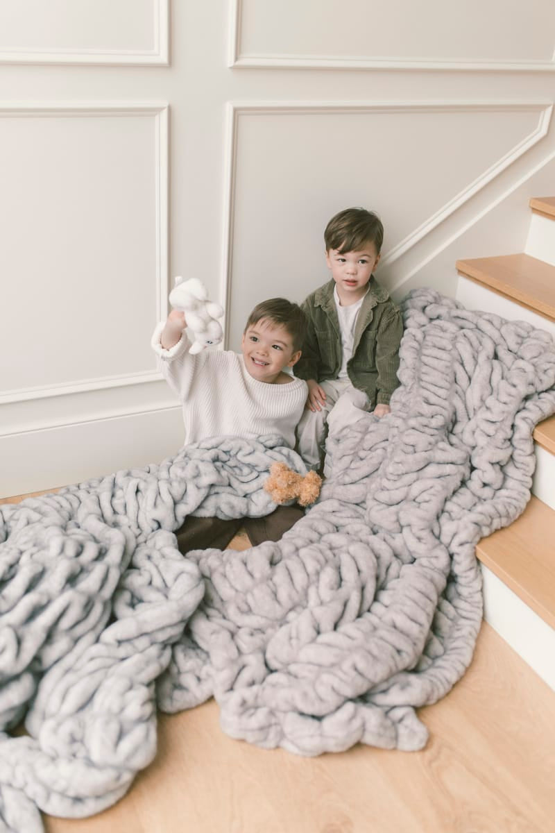 Two children sitting on a staircase wrapped in a two gray blankets.