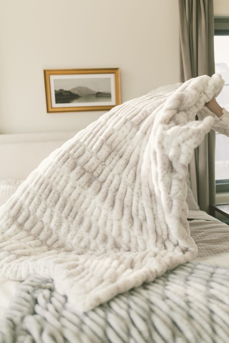 Cozy white textured blanket draped over a bed in a bedroom setting.