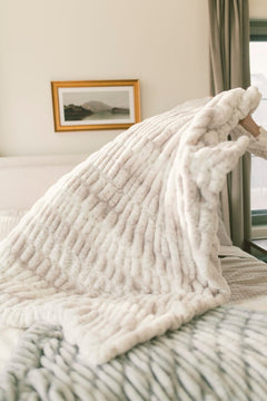 Cozy white textured blanket draped over a bed in a bedroom setting.