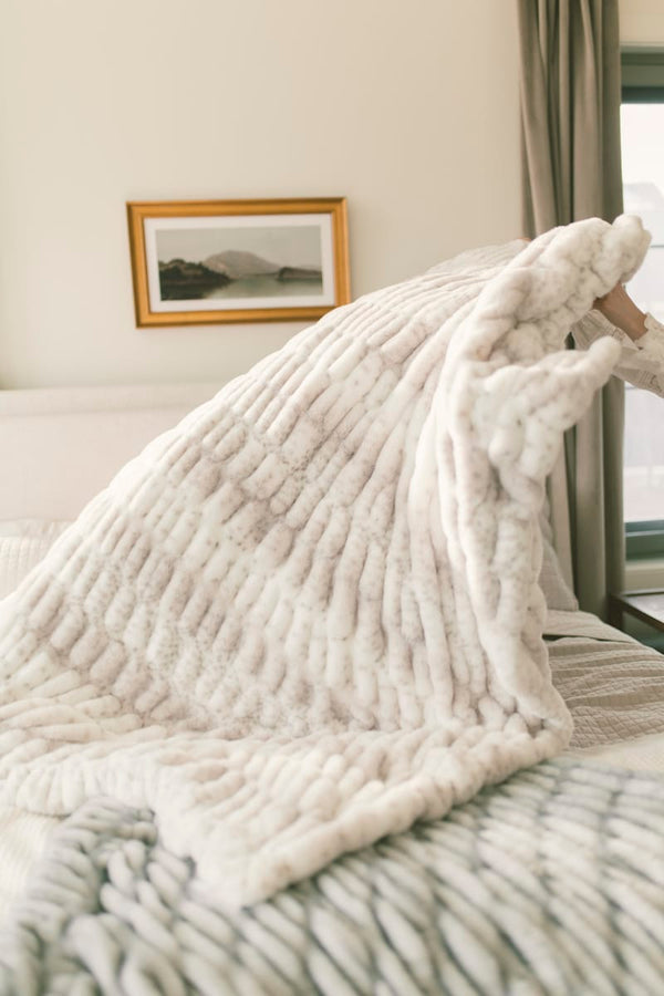 Cozy white textured blanket draped over a bed in a bedroom setting.