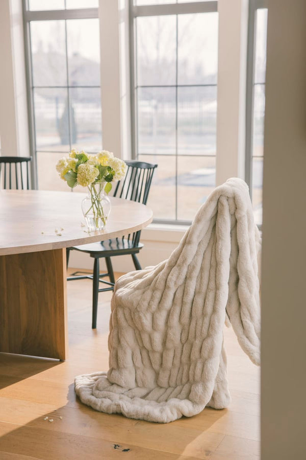 Beige textured blanket draped over a chair in a room with large windows.