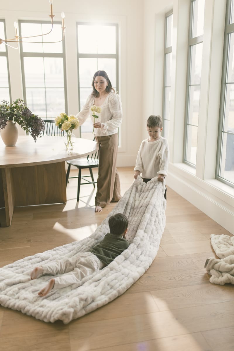 Two little boys playing with a large cream blanket in the kitchen.
