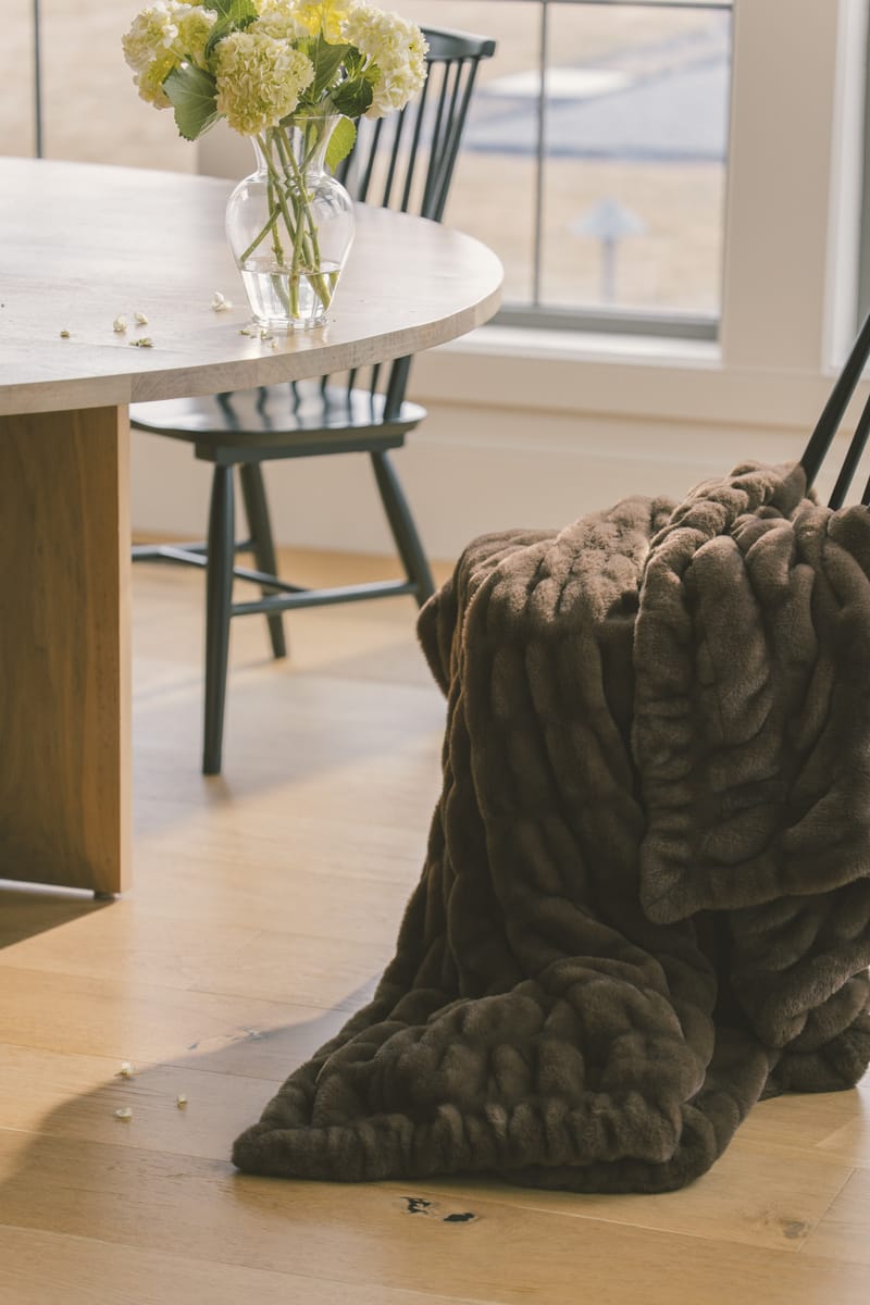 Hugs Hot Fudge Blanket draped over a chair in a stylish indoor setting, showcasing its cozy brown design.