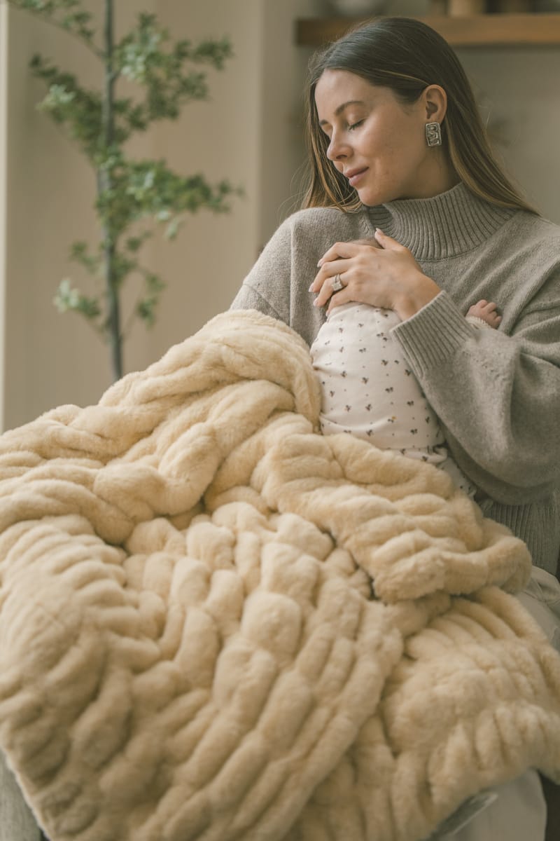 Woman holding a baby wrapped in a yellow Hugs Honey Butter Blanket indoors.
